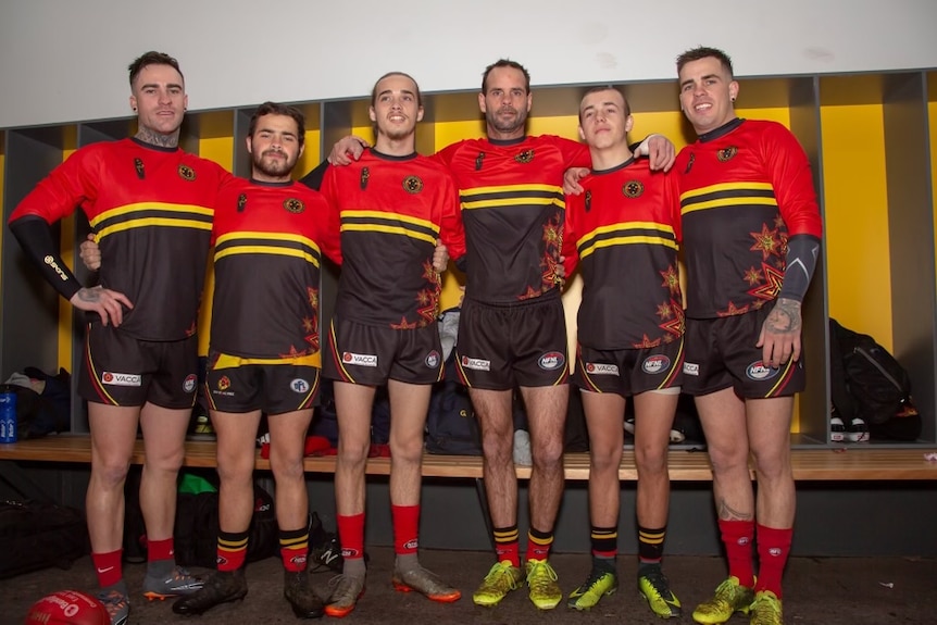 Group of AFL players with their hands around one another smiling for a photo in their team uniform