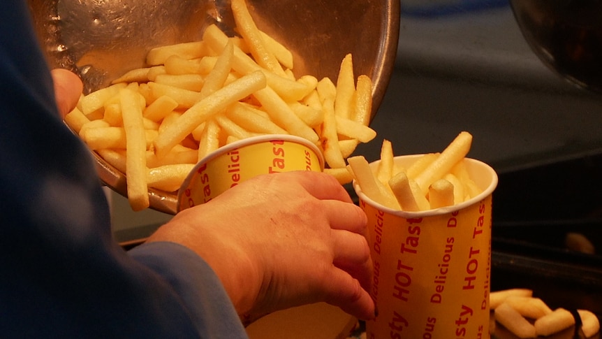 A scoop of hot chips is loaded into a fast food container.