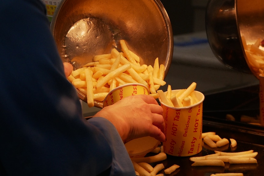 A scoop of hot chips is loaded into a fast food container.