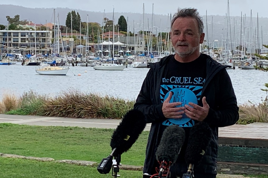 A man speaks to the media by the waterfront.