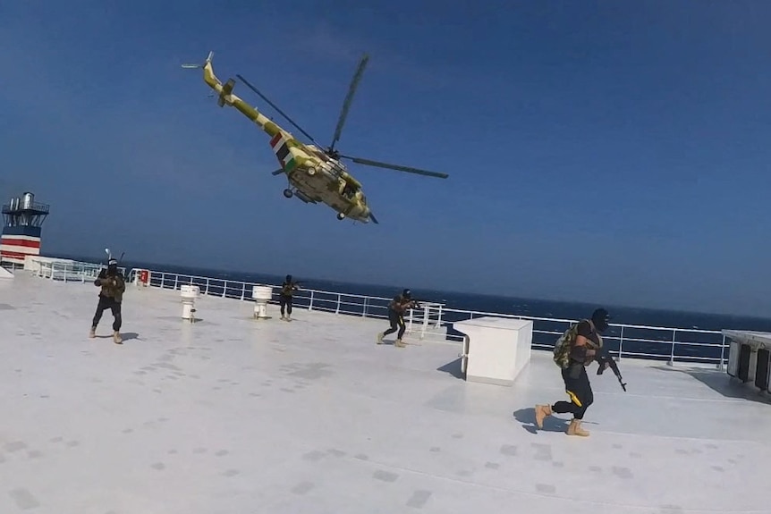 A helicopter flies over a large ship with four gunmen with covered faces running on deck