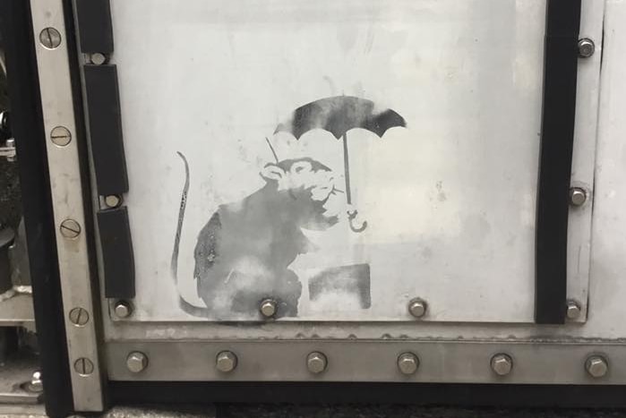 A spray-painted image of a rat holding an umbrella.