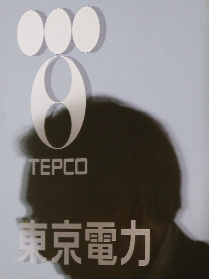 A man is reflected in a glass door with a logo of Tokyo Electric Power Co (TEPCO)