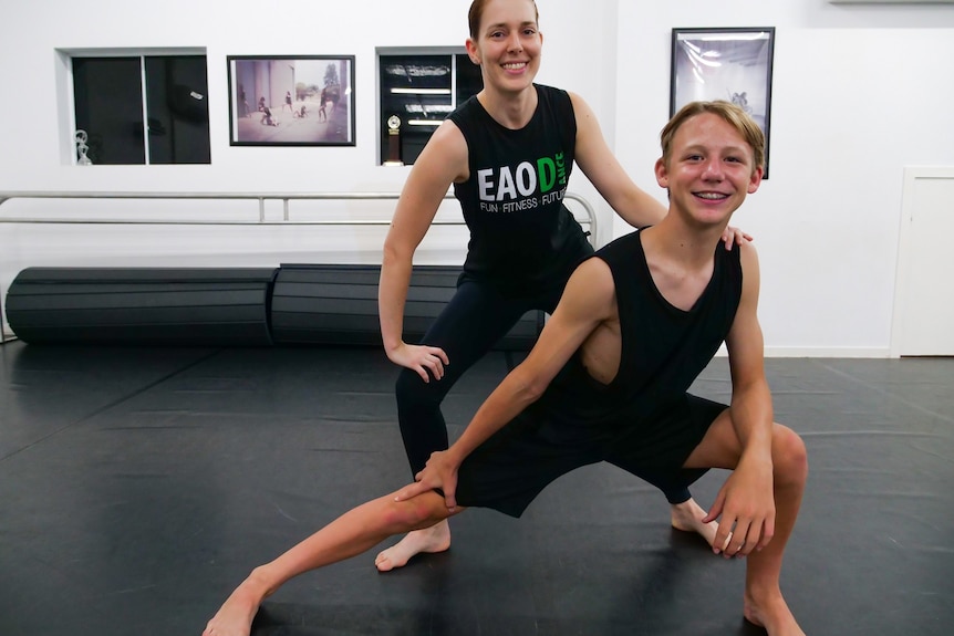 Two dancers in black and hold a pose together in a dance studio
