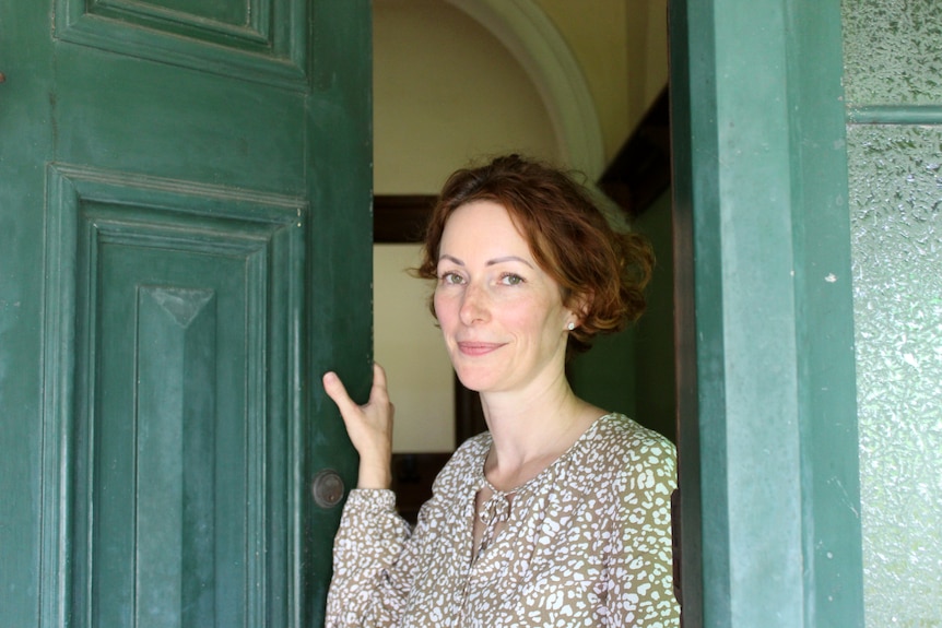 A smiling woman standing in a dark green doorway.