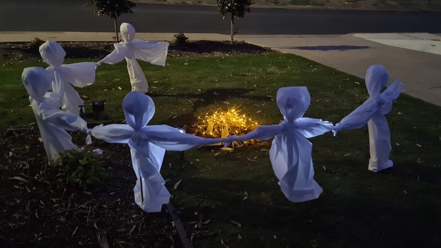 Ghosts made of white fabric standing around a campfire in a front garden