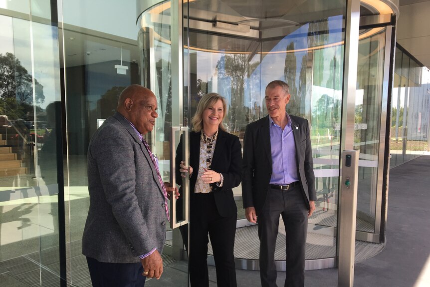 Two men and a women standing outside revolving glass doors of a building