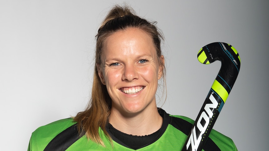 Hockey players dressed in her team uniform with hockey stick in her hand smiling for a photo