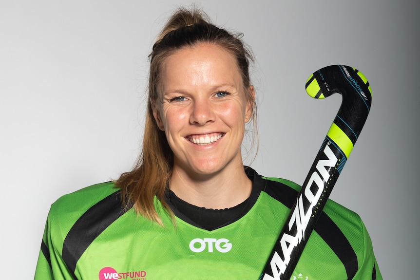 Hockey players dressed in her team uniform with hockey stick in her hand smiling for a photo
