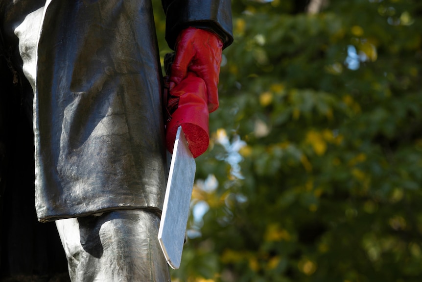 A statue's hand painted red, holding a fake saw