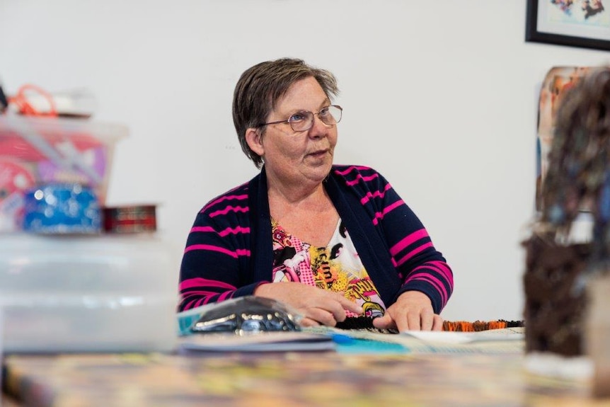 Merynda wearing a black cardigan with pink stripes, while sitting at a table working on craft.