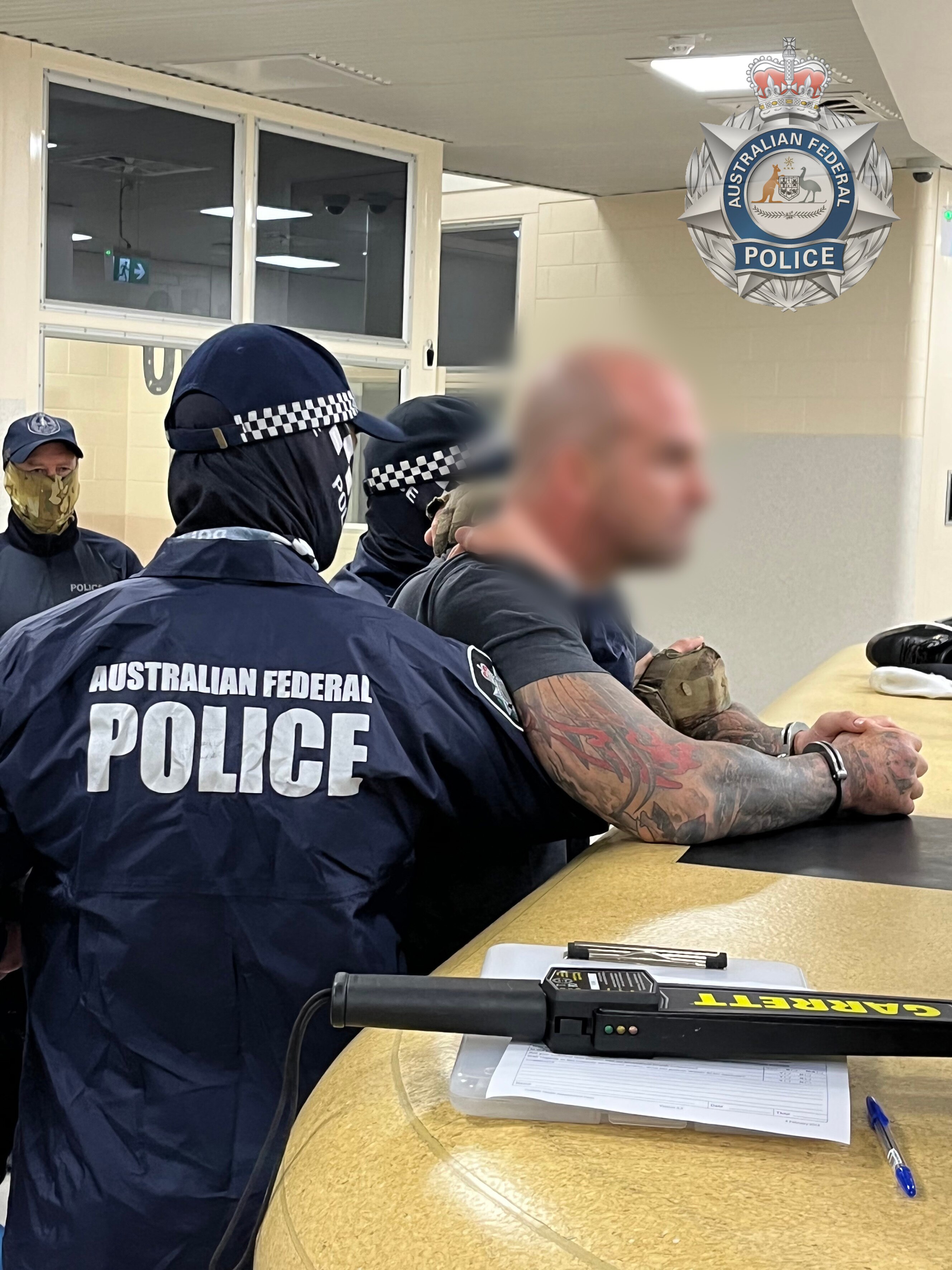 A man in surrounded by Australian Federal Police officers, some of whom are holding him around the chest.  His face of him is blurred.
