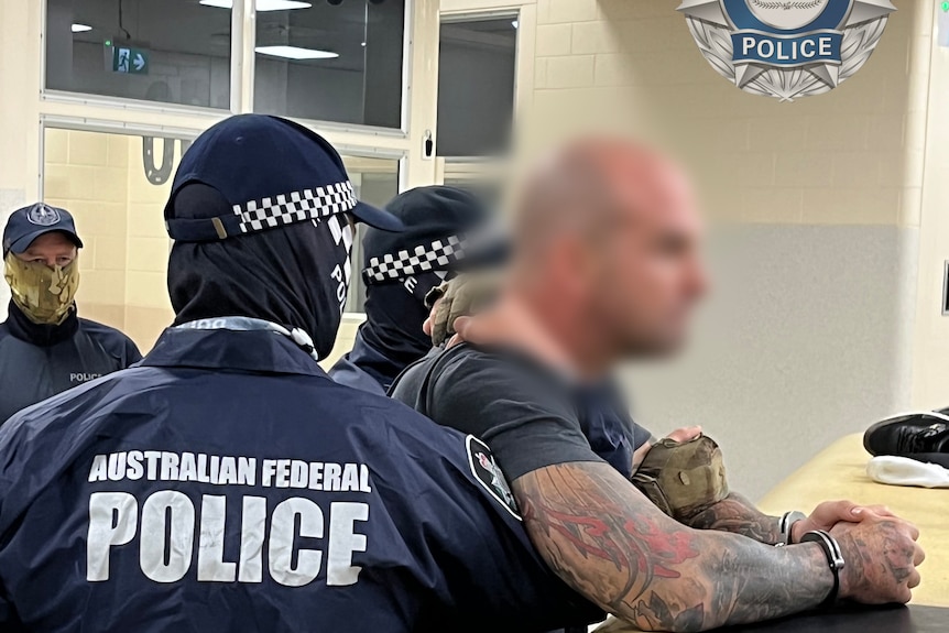 A man in surrounded by Australian Federal Police officers, some of which are holding him around the chest. His face is blurred.