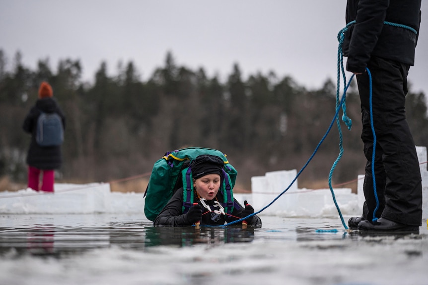 A primary school child in heavy winter clothes wades in a frozen lake.