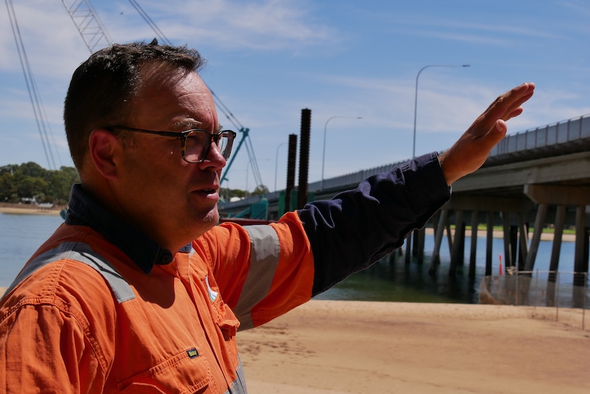 A man with glasses and a hi-visibility shirt waving to the Joy Baluch Bridge 