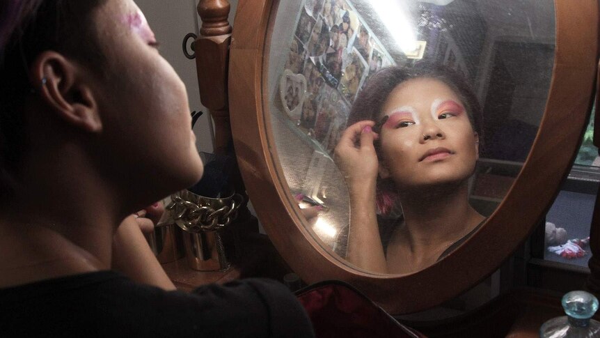 woman looking in a mirror putting on pink eye makeup