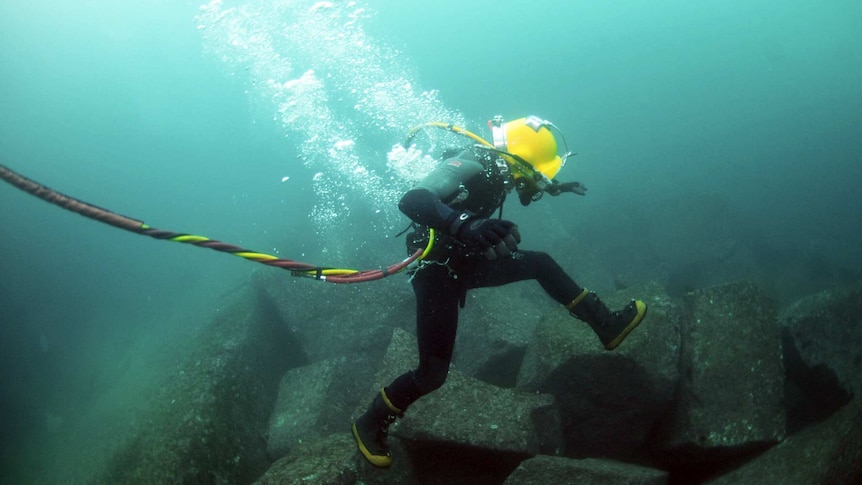 A US Navy diver leaps from rock to rock along the ocean floor during diving operations.