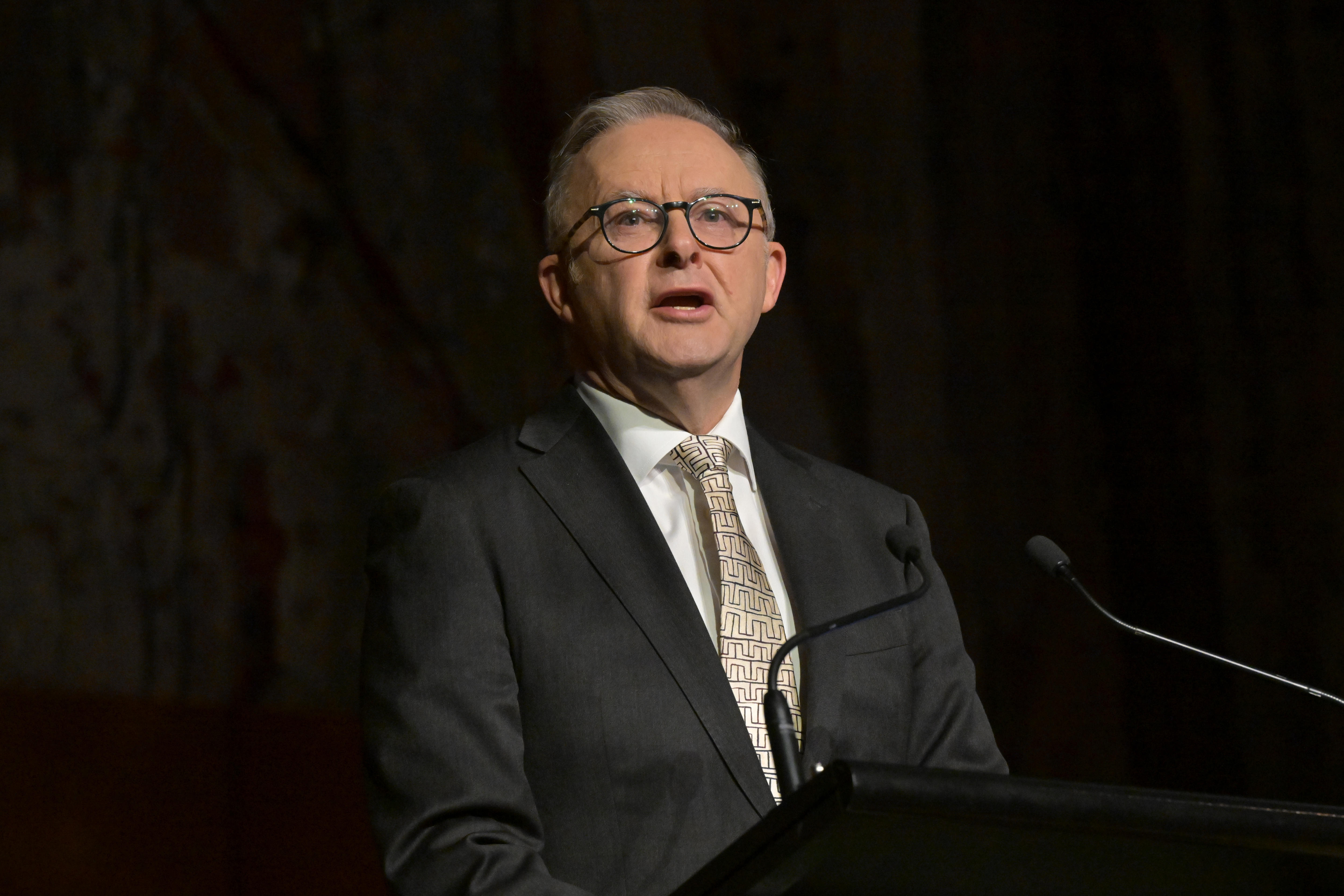 A man in a suit and tie stands at speaks at a lecturn.