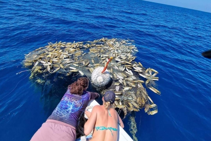 Two women lay on the bow of a boat, recovering a net filled with plastic and sea life.