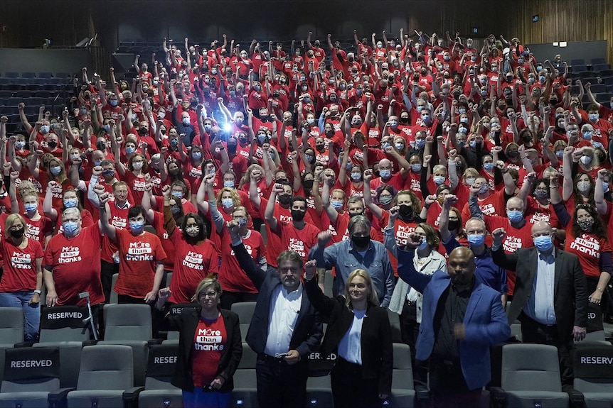 A large crowd of teacher union members wearing red shirts and raising their hands in the air.