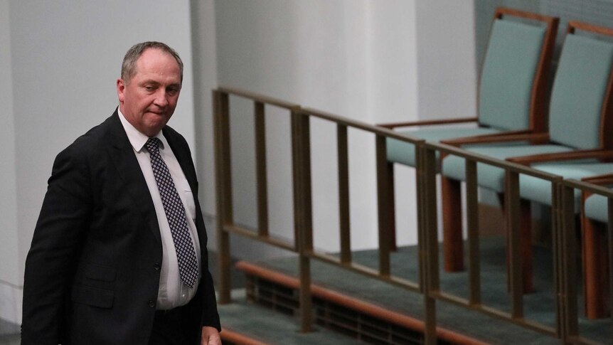 Barnaby Joyce, with an angry expression, walks past empty chairs