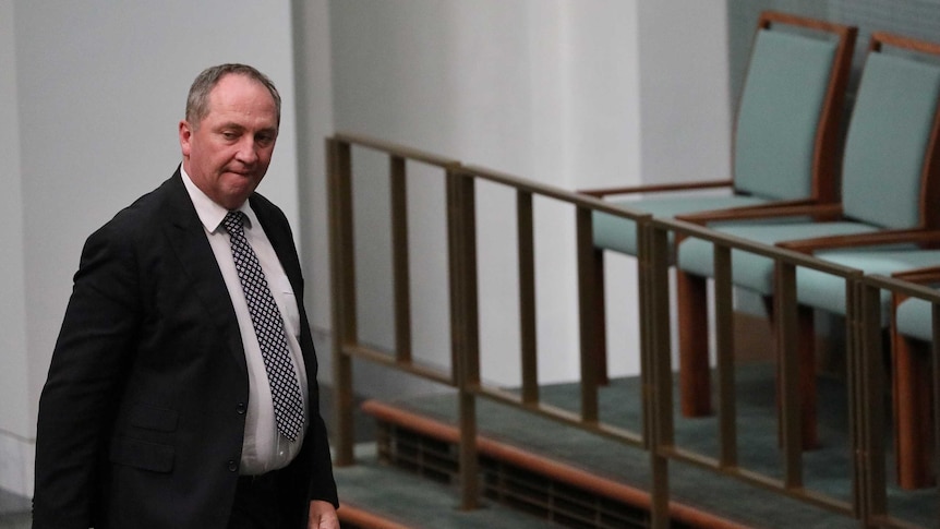 Barnaby Joyce, with an angry expression, walks past empty chairs