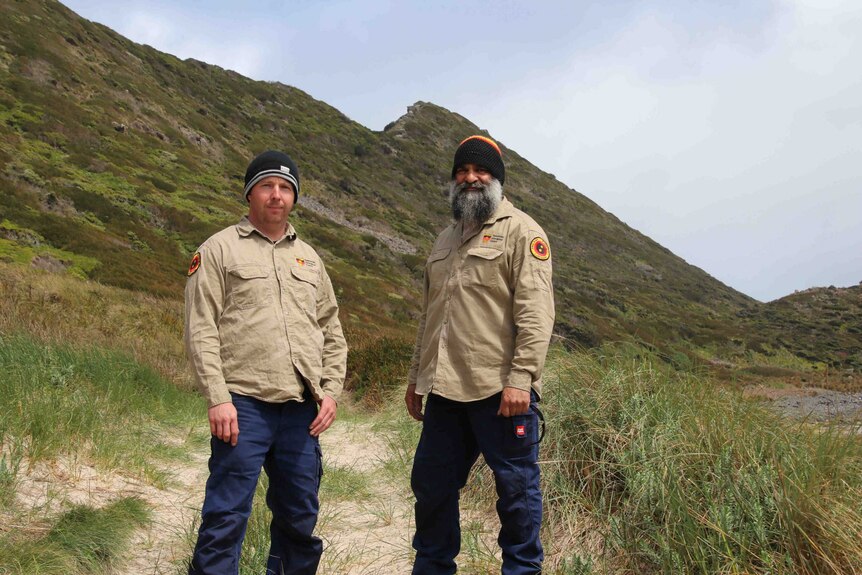 Two men in ranger uniforms pose for a photo near beachy terrain