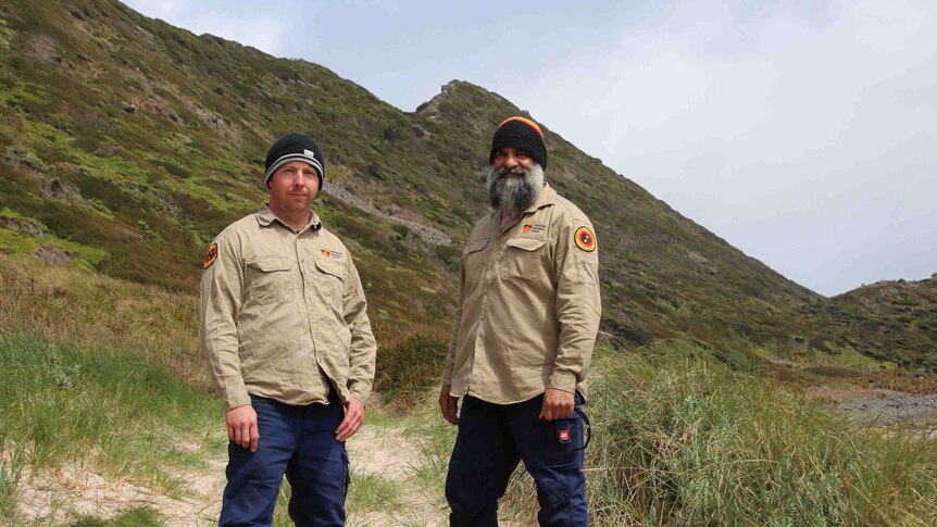 Two men in ranger uniforms pose for a photo near beachy terrain