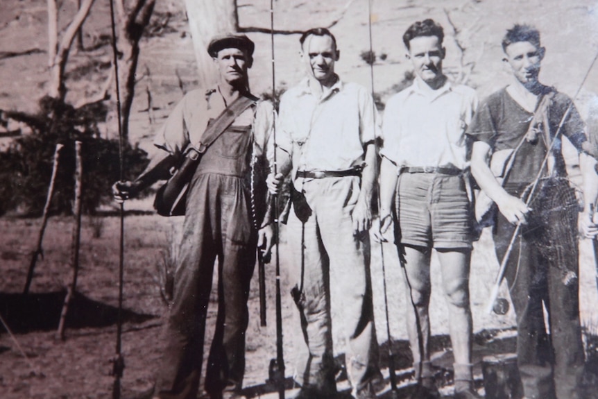 An aged photo of five men standing alongside each other while holding fishing rods.