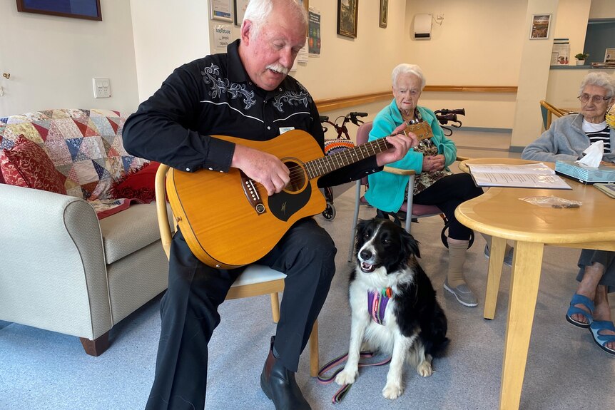 A man holds a guitar and sits next to a dog