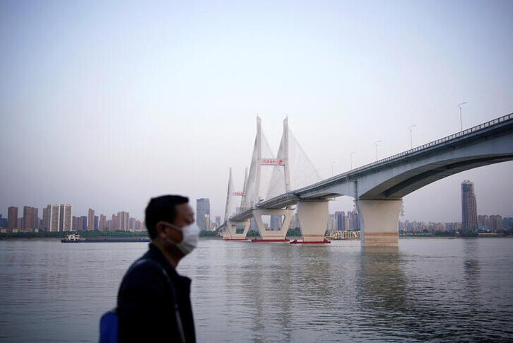 A man wearing a face mask is pictured with a bridge in Wuhan in the background.