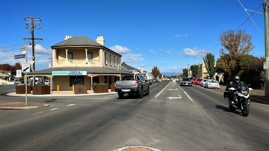 Main street of a small town with a pub on the left and a motorbike driving down the road