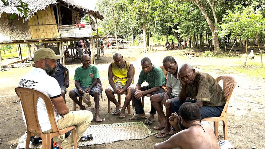 Men sit around in a semi circle to talk in a village in Papua New Guinea.