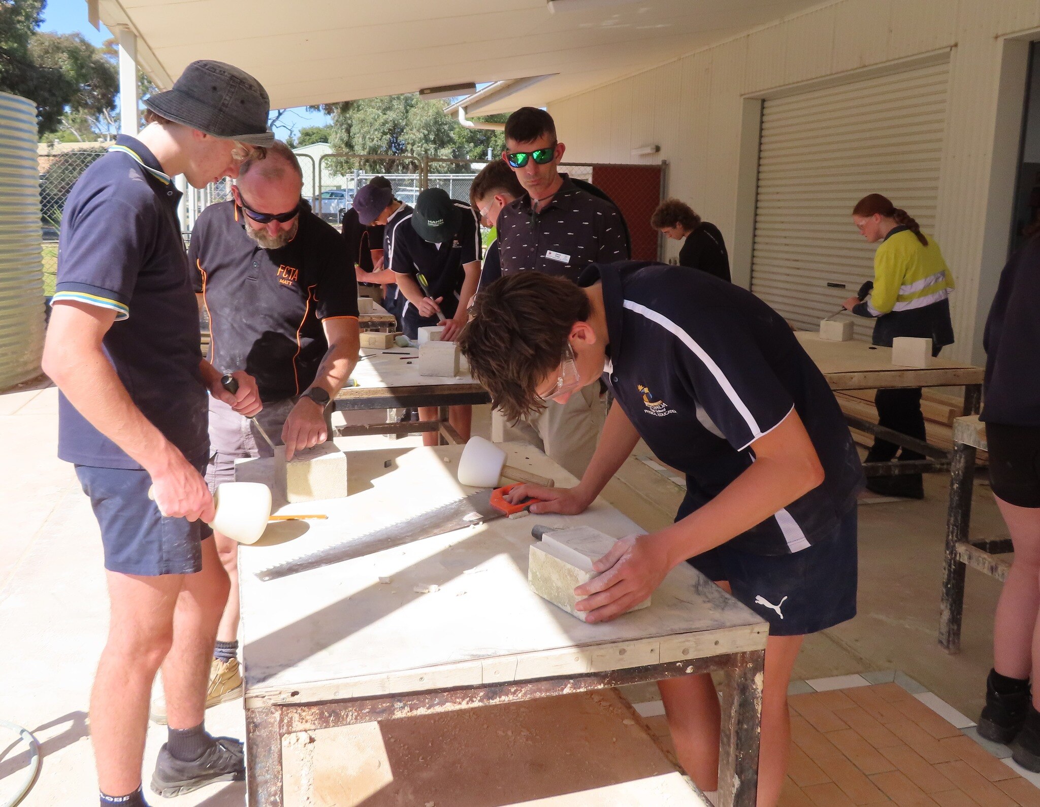Teenagers leaning over a table using tools to do stone masonry.