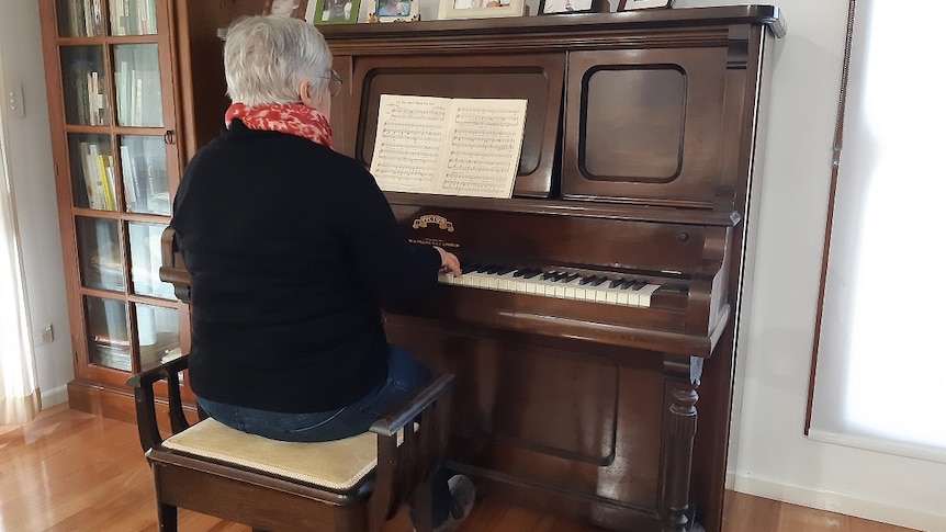 A woman with short grey hair plays her piano in her living room