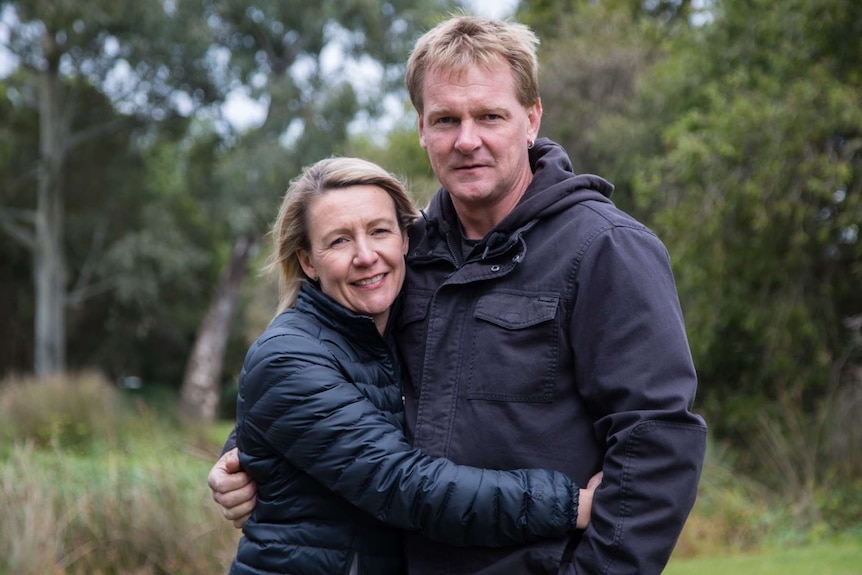 Danielle and Darryl Squires in a park, hug as they look at the camera.