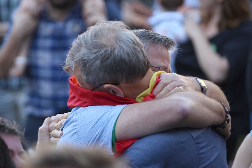 Mandurah couple Neil Connery and Geoff Bishop hug with flags around their necks.