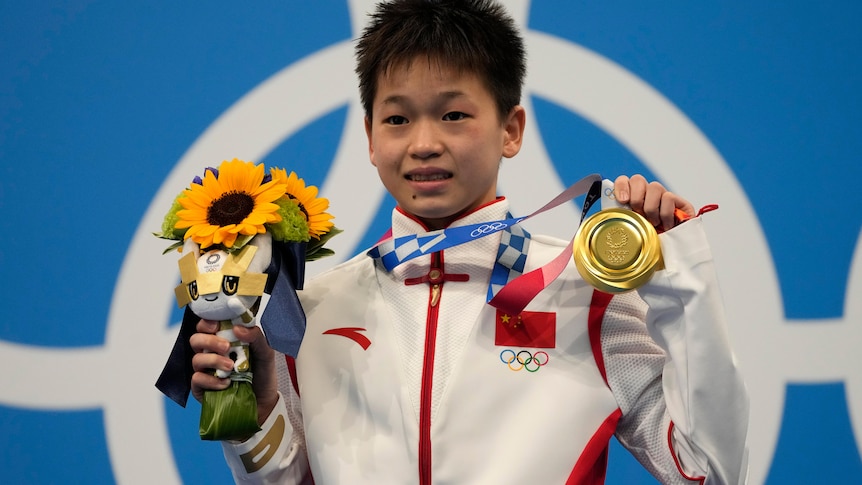 An athlete poses with her gold medal and a bunch of flowers