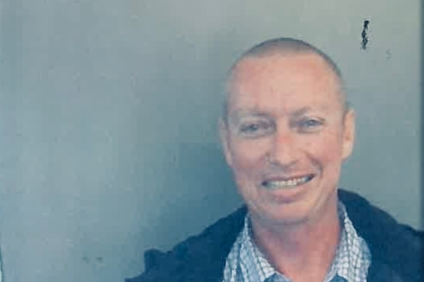 Convicted sex offender Peter John van de Wetering smiling in front of a grey wall