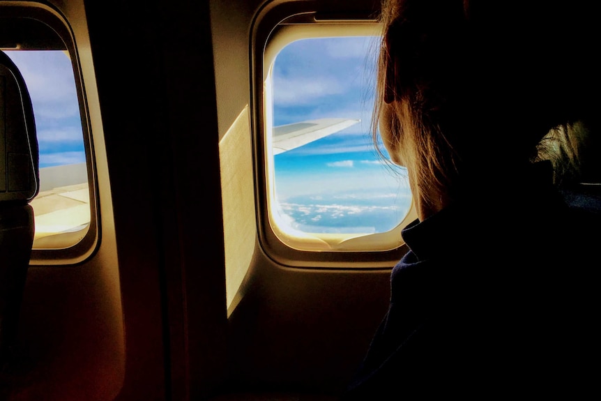 A photograph of someone on a plane, gazing out the window at the blue sky.