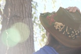 a woman wearing a hat is starting at a large tree with her back to the camera