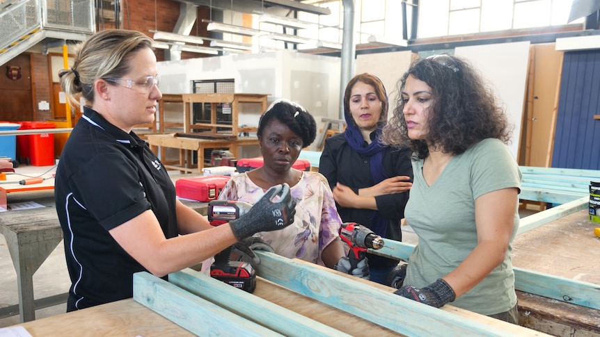 women listening to their teacher who is showing them how to use a power tool