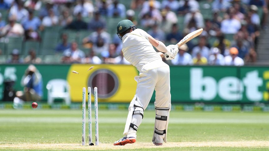 Australian batsman Travis Head is seen from behind, swinging his bat as the ball hits his stumps during a Test at the MCG.