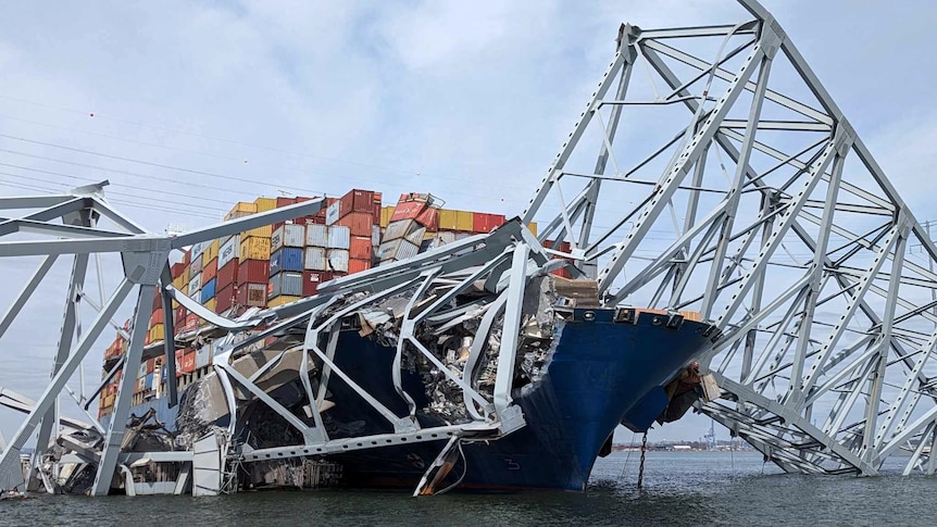 Part of the steel bridge span is smashed on top of a loaded cargo ship.