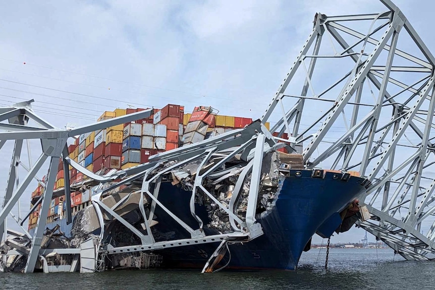 Part of the steel bridge span is smashed on top of a loaded cargo ship.