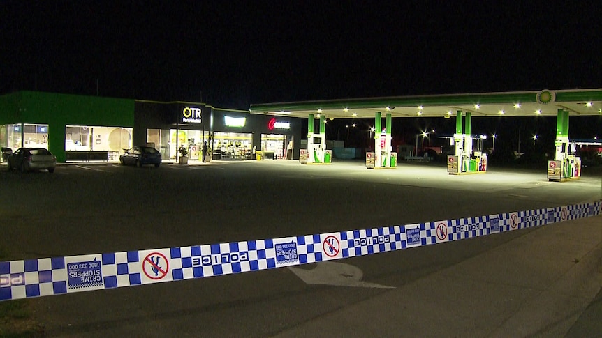 Police tape stretching across the foreground with a service station in the background at night