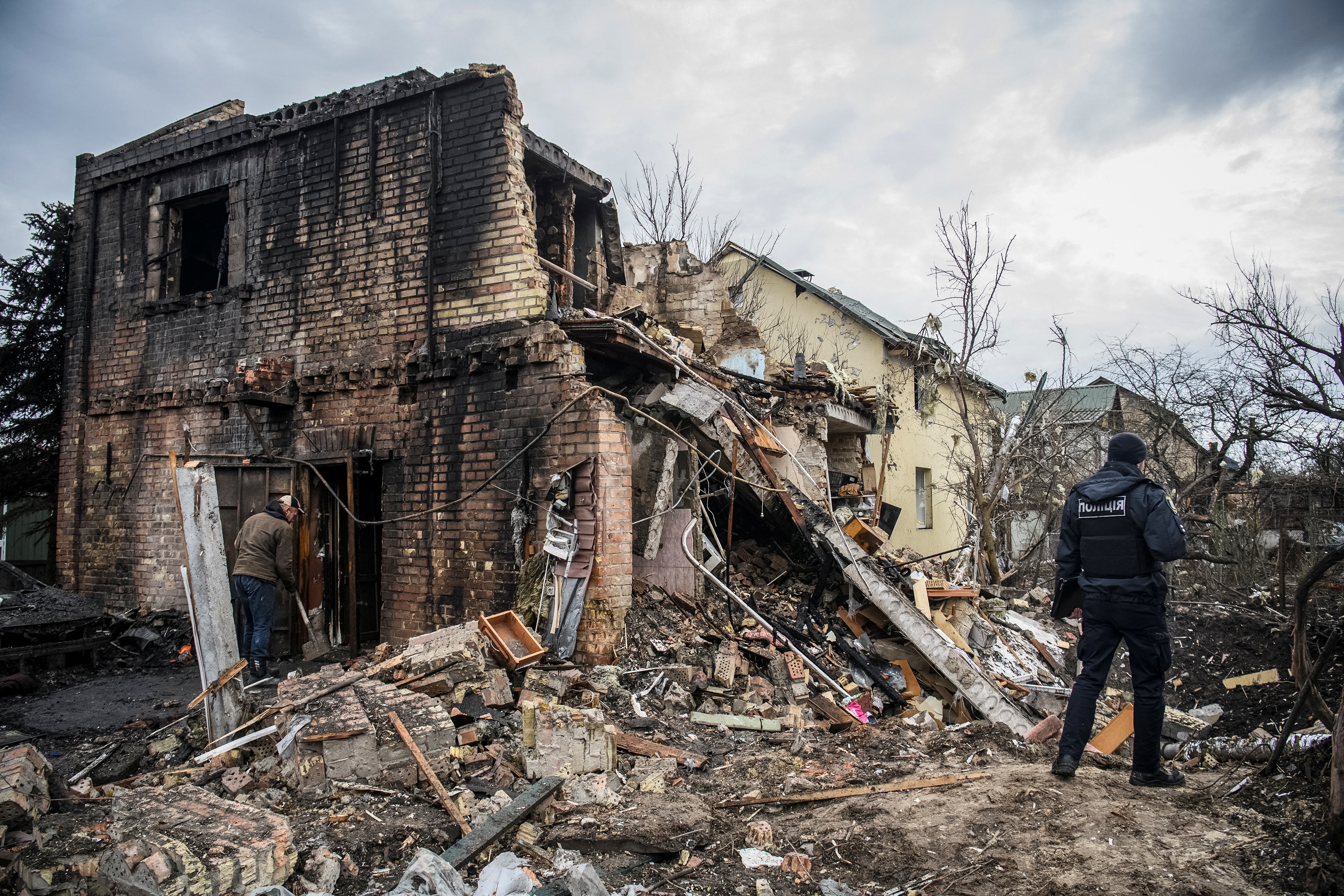 Man stands beside house destroyed by missile strike.