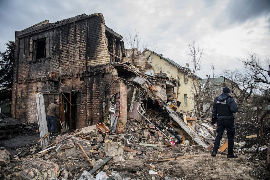 Man stands beside house destroyed by missile strike.