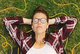 A woman lies on grass while wearing headphones.