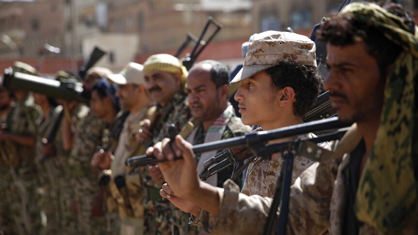 Houthi rebel fighters hold up their weapons as they stand in a row.